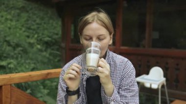 Caddedeki bir dağ kafesinde oturup cam bardaktan latte içen bir kadının yakın çekimi. Ojcowski Parkı