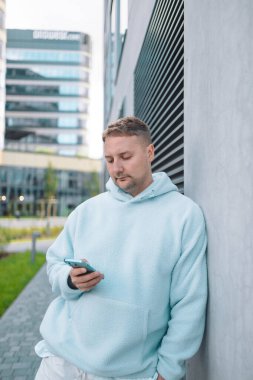 Güler yüzlü iş adamı şehir merkezinde telefonla dışarıda dolaşıyor. İş ortamında modern yaşam tarzı, iletişim ve teknolojiyi yansıtan kendine güvenen erkek akıllı telefon.