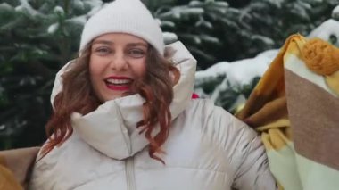 Kış ormanındaki karlı ağaçların arasında ilk karın tadını çıkaran mutlu bir kadın. Şapka ve eşarplı genç bir kadın kış ormanında eğleniyor. Yaşam biçimi. 