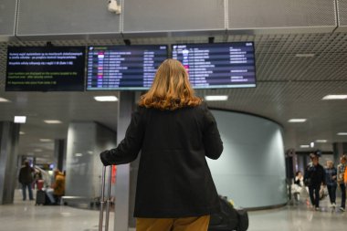 Uluslararası havaalanındaki genç beyaz kadın, cep telefonu kullanıyor ve uçuş saatlerini, uçuş saatlerini, havaalanına varış ve kalkış saatlerini kontrol ediyor..