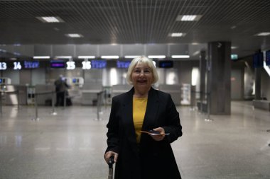 Traveler tourist happy smiling joyful fun mature elderly senior lady woman 55 years old with hand luggage, backpack holds passport and waits for flight travel at international airport terminal.  clipart