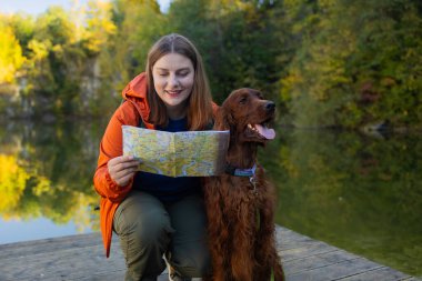 Mutlu bir kadın ve bir köpeğin haritaya baktığı ve planlama yaptığı bir fotoğraf ya da yazın ormanda bir sonbahar gölünün kenarında sırt çantasıyla otururken kaybolmak. Yüksek kalite fotoğraf