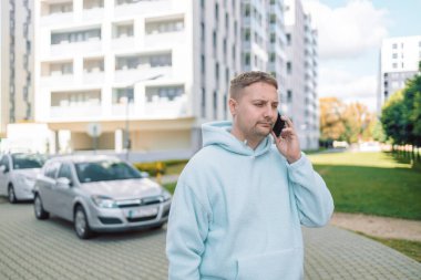 Moda kıyafetli, yakışıklı, beyaz sakallı, üzgün bir adam. Şehir sokağında telefonla konuşuyor ve gün ışığında başka tarafa bakıyor. Yüksek kalite fotoğraf