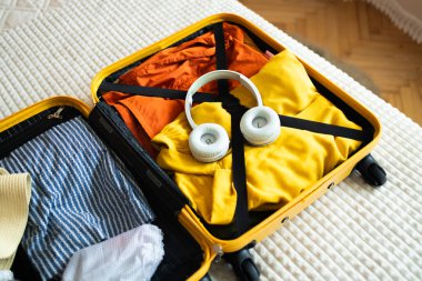 Açık sarı bavul, farklı aile kıyafetleri ve aksesuarlarla aydınlık yatak odasında. Bagajlar yolculuk için hazırlanıyor, boşluğu kopyala. 