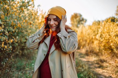 Merhaba Ekim. Sonbahar parkında ceketli, neşeli, moda tarzlı, uzun kahverengi saçlı çekici genç bir kadın. Yüksek kalite fotoğraf