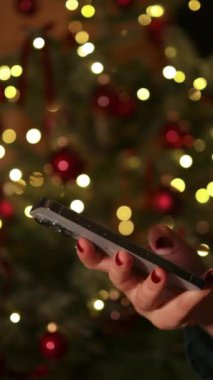 4k Woman akıllı telefonu 2025 yılbaşı Noel tatilinde evde ya da alışveriş merkezinde tutuyor. Noel indirimi, satış ve promosyon için çevrimiçi mağazadan kadın alışverişi. Dikey video