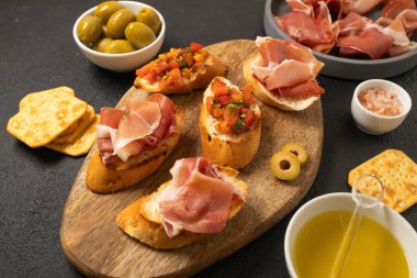 Zeytinli sandviç, kepek ekmeği, vişneli domates, ahşap kesim tahtasında jambon, koyu siyah arka plan.