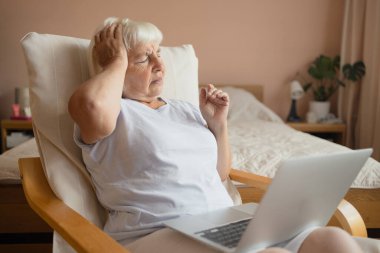 Evde dizüstü bilgisayarla oturan, yaşlı, tatminsiz emekli bir kadının portresi. Duygusal, sinirli yaşlı bir kadın dizüstü bilgisayarına bakar ve kaşlarını çatar.. 
