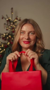 20 'li yaşlarda güzel bir kadının portresi yeni yıl için kırmızı alışveriş çantası taşıyor. Noel' i kutlamak için iç mekanda süslenmiş Noel ışıkları. Kadın, kış tatilini kutlamaya hazır hediyeler taşıyor. 