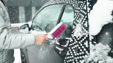 Karla kaplı bir araba. Bir adam özel fırçalarla arabayı kardan temizler. Soğuk bir hava. Yüksek kaliteli FullHD görüntüler
