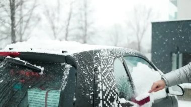 Karla kaplı bir araba. Bir adam özel fırçalarla arabayı kardan temizler. Soğuk bir hava. Yüksek kaliteli FullHD görüntüler