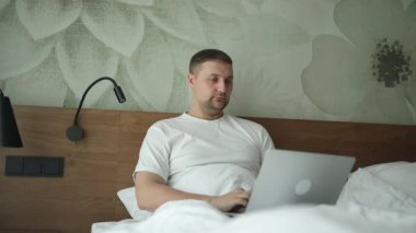 Otel Oda veya ev yatak odasında dizüstü bilgisayar kullanan adam. Yatakta yatarken ve tipik dizüstü bilgisayar ile adam. İleti e-posta okuma ve gönderme, modern cihaz sabah bizzat. Evde çalışma kavramı