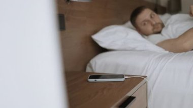 Yatakta uyuyan yakışıklı beyaz adam akıllı telefon çalar saati ile uyandı.. 