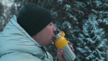 Yakından çekilmiş portre yakışıklı sakallı beyaz adam kışlık giysiler içinde ve termosuyla açık havada Çek kraker yiyor. Soğuk mevsim ve kışın sıcak içecek 