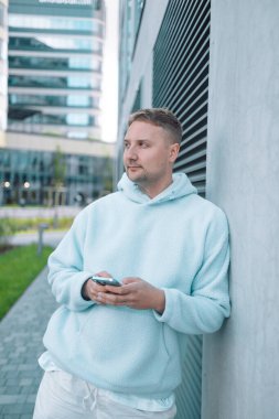 Güler yüzlü iş adamı şehir merkezinde telefonla dışarıda dolaşıyor. İş ortamında modern yaşam tarzı, iletişim ve teknolojiyi yansıtan kendine güvenen erkek akıllı telefon.