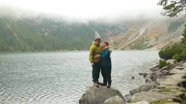 Sırt çantalı iki genç turist, Morskie Oko, Yüksek Tatra Dağları ve Poland 'dan gelen patikadaki Czarny Gölü' nün ortasındaki büyük bir kayanın üzerinde duruyor. Genç adam.