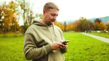 Şehir parkının yakınlarında günlük giysiler içinde yürüyen yakışıklı, mutlu sakallı bir öğrenci. Mutlu yakışıklı sakallı erkek mesajlaşması, e-postaları kontrol etme, internette sohbet etme, sosyal medyada gezinme. Yüksek kalite FullHD