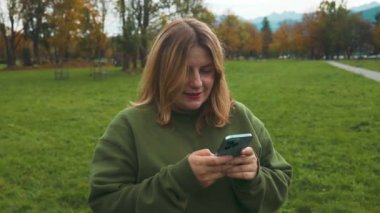 Dışarıda cep telefonuna bakan gülümseyen bir kadın. Şehirde akıllı telefon kullanan genç beyaz bir kadın var. Teknoloji, bağlantı, iletişim, modern yaşam tarzı kavramları. Yüksek kaliteli FullHD görüntüler
