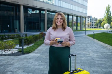 Kafkasyalı 30 yaşında iş kadını akıllı telefon kullanıyor seyahat çantası, akıllı telefon kullanıyor, ulaşımı bekliyor, dışarıda bekliyor.