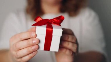 Elinde kurdele olan hediye kutusu tutan bir kadın. Kadın ayağa kalk ve kırmızı kurdeleli beyaz hediye kutusunu göster. Sevgililer günü, doğum günü, aşk ve kutlama konsepti