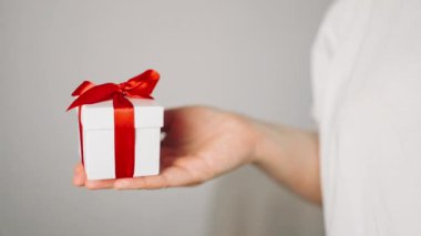 Elinde kurdele olan hediye kutusu tutan bir kadın. Kadın ayağa kalk ve kırmızı kurdeleli beyaz hediye kutusunu göster. Sevgililer günü, doğum günü, aşk ve kutlama konsepti