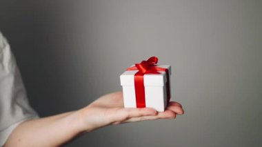 Elinde kurdele olan hediye kutusu tutan bir kadın. Kadın ayağa kalk ve kırmızı kurdeleli beyaz hediye kutusunu göster. Sevgililer günü, doğum günü, aşk ve kutlama konsepti