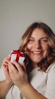 30 'lu yılların güzel kızı hediye kutusunu sallıyor ve içinde doğum gününü kutlarken ne olduğunu merak ediyor, doğum günü hediyeleri alıyor. Tatiller, kutlamalar ve kadın konsepti. Yüksek kaliteli FullHD görüntüler