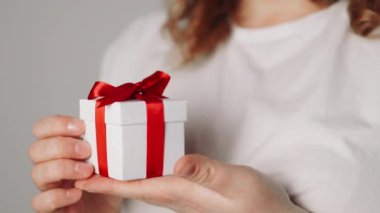 Elinde kurdele olan hediye kutusu tutan bir kadın. Kadın ayağa kalk ve kırmızı kurdeleli beyaz hediye kutusunu göster. Sevgililer günü, doğum günü, aşk ve kutlama konsepti