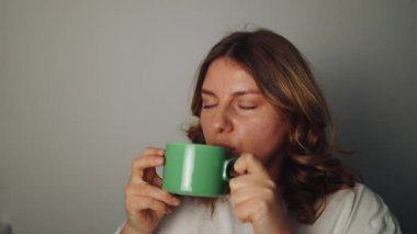 Hafta sonu sıcak bir oturma odasında sıcak bir fincan kahve ya da çay içen genç bir kadın. Yüksek kaliteli FullHD görüntüler