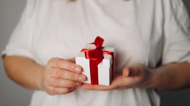 Elinde kurdele olan hediye kutusu tutan bir kadın. Kadın ayağa kalk ve kırmızı kurdeleli beyaz hediye kutusunu göster. Sevgililer günü, doğum günü, aşk ve kutlama konsepti
