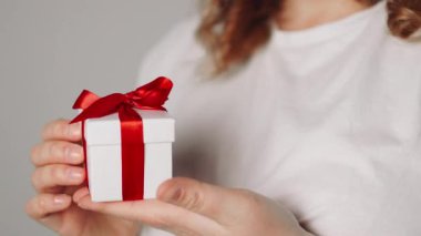 Elinde kurdele olan hediye kutusu tutan bir kadın. Kadın ayağa kalk ve kırmızı kurdeleli beyaz hediye kutusunu göster. Sevgililer günü, doğum günü, aşk ve kutlama konsepti