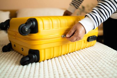 Beyaz kadın elbiselerini sarı bavula koyup tatil gezisi için çantalarını kilitlemeye çalışıyor, yaz yolculuğuna hazırlanıyor. Seyahat kavramı
