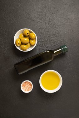 Beyaz kasede zeytinyağı ve zeytin yağı ve koyu arkaplanda bir şişe zeytin yağı. Paket için maket. Uzayı kopyala Yüksek kalite fotoğraf