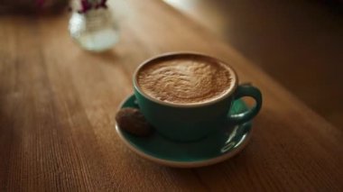 Yeşil tabakta kaşık ile servis edilen kremalı sütlü bir fincan kahve. Kahve dükkanındaki ahşap bir masada birkaç tabak. Bir kupa sütlü kahve, kapuçino..