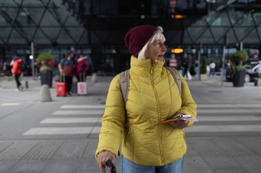 Gezgin olgun yaşlı kadın 60 yaşında şık kıyafetler giyiyor. Çantayı havaalanına yakın bir yerde tutuyor.