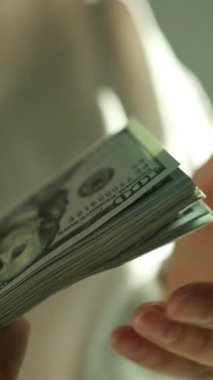 Vergi belgelerini incelerken 100 dolarlık banknotlar sayan bir kadın. Finansal planlama ve vergi hazırlama kavramı. Dünya ekonomisi. Döviz bürosu. Nakit ödeme. Yüksek kaliteli FullHD görüntüler