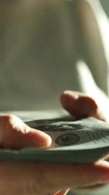 Vergi belgelerini incelerken 100 dolarlık banknotlar sayan bir kadın. Finansal planlama ve vergi hazırlama kavramı. Dünya ekonomisi. Döviz bürosu. Nakit ödeme. Yüksek kaliteli FullHD görüntüler