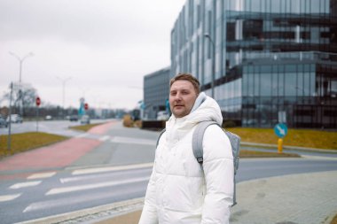 30 'lu yaşlarda, sırt çantalı beyaz bir adam zebra karşıya geçerken sokakta bulanık arabaları kullanıyor.