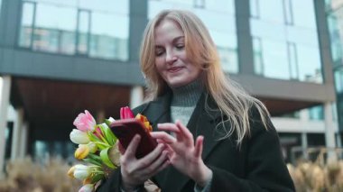 Dünya Kadınlar Günü 'nde çantalı ve çiçekli akıllı bir telefon kullanan beyaz bir kadın..