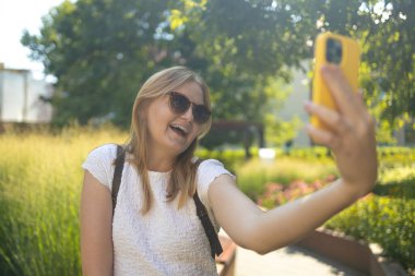 Şehir parkında selfie çeken şık gülümseyen 30 'lu yaşlardaki bayan yürüyüş yaparken kendi portresini çeken mutlu genç bayan ve dışarıda dinlenen iyi günler.
