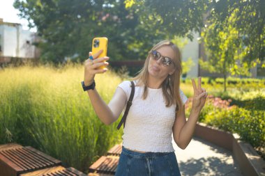 Şehir parkında selfie çeken şık gülümseyen 30 'lu yaşlardaki bayan yürüyüş yaparken kendi portresini çeken mutlu genç bayan ve dışarıda dinlenen iyi günler.
