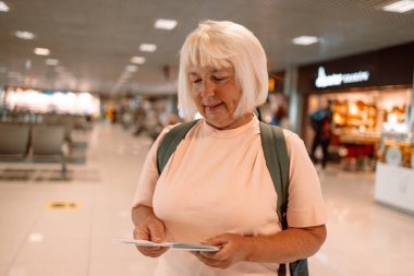Havalimanında turistin pasaport kontrolünü beklerken sırt çantalı ve pasaportlu mutlu sarışın yaşlı bayan turist. Yüksek kalite fotoğraf