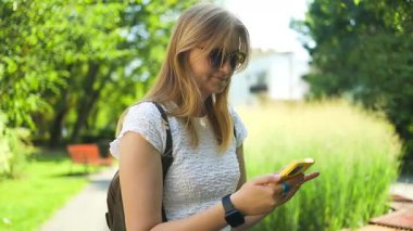 Yakın plan çekimde, açık havada bir bankta oturan ve akıllı telefonunu, insan yaşam tarzını ve kablosuz teknoloji kavramlarını kullanan bir kadın görülüyor. Yüksek kalite fotoğraf