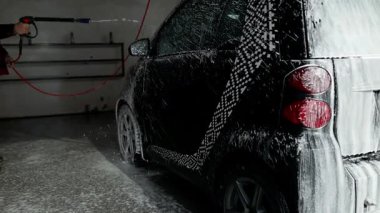 Dış araba temizliği. Araba yıkama istasyonunda beyaz sabun köpüğüyle araba tekerleğini kapat, deterjanla profesyonel araç temizliği yap. Otomobili köpükle kaplayan adam dışarıda araba yıkamada.