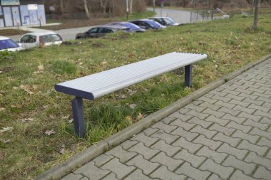 Yürüyüş yolu boyunca ahşap bir bankın olduğu huzurlu bir park sahnesi. Kamu parkındaki ağaçların ve yeşilliğin tadını çıkarırken bank dinlenmek için bir yer sağlıyor.