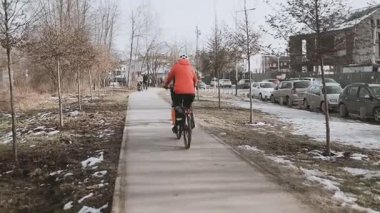 Güneşli bir kış gününde, bir şehir parkında karla kaplı ağaçların arasında bisiklet yolu boyunca bisiklet süren bir bisikletçi. Kışın aktif bir yaşam tarzı. Çevre dostu ulaşım. 