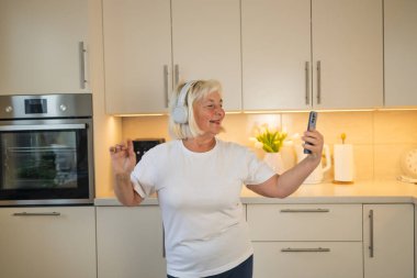 Son sınıf öğrencisi bir kadın mutfağında duruyor, gülümsüyor ve en sevdiği müziğin tadını çıkarıyor. Telefonundan melodileri dinliyor, rahat evindeki o anın mutluluğunu kucaklıyor.
