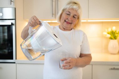 Mutfakta elinde bir sürahi ve bir bardak tutan mutlu bir son sınıf öğrencisi, kendine ferahlatıcı bir içki koymaya hazır. Bu görüntü evdeki sağlıklı alışkanlıkları ve keyifli anları yansıtıyor.