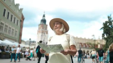 Bir şehirde elinde haritayla gezen ve akıllı telefondan yol tarifini kontrol eden yaşlı bir kadın. Sarı bir sırt çantası ve şapkası olan yeni bir yer keşfediyor. Mutlu gezgin yolculuğun tadını çıkarıyor..