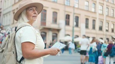 Bir turist kadın bir harita tutuyor ve hareketli kalabalıklar ve arka planda güzel bir mimariyle işlek bir şehir caddesini keşfediyor. Görüntü, şehir seyahatinin ve keşiflerin özünü yakalıyor.